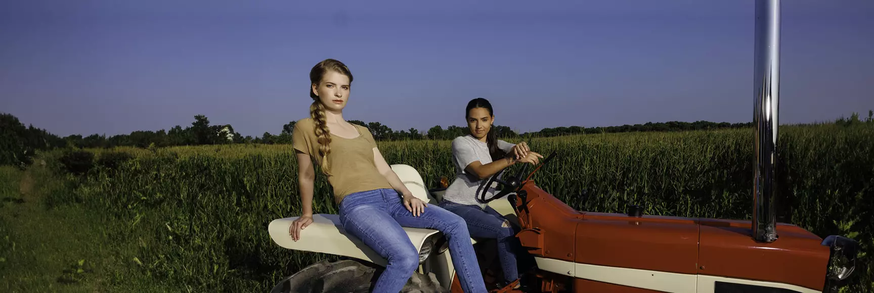 Two models wearing blue jeans on a tractor in a cornfield