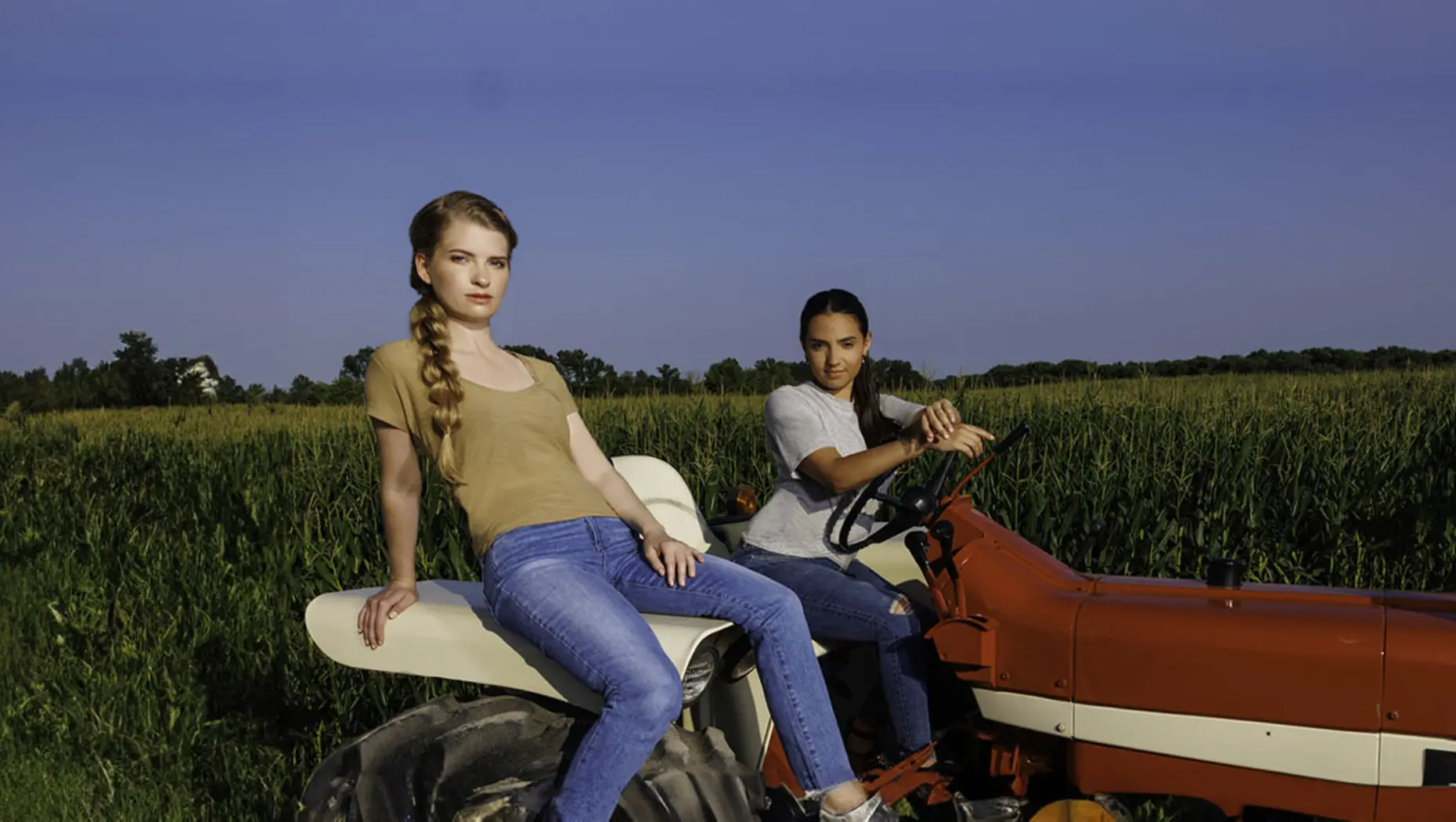 Two models wearing blue jeans on a tractor in a cornfield